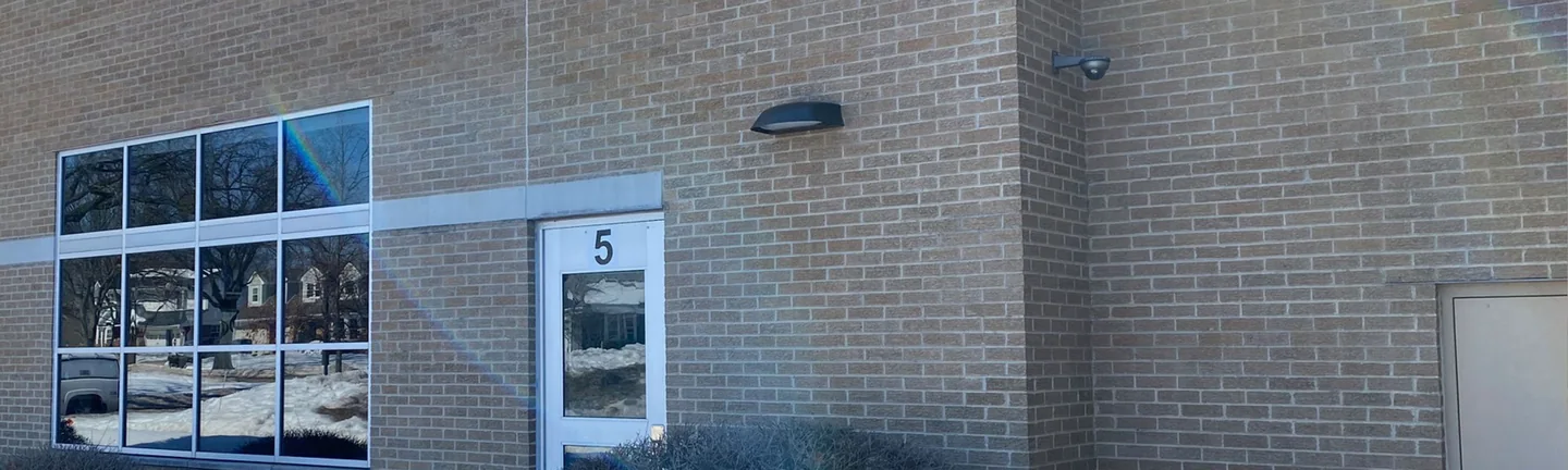 The tan bark textured brick of the school in Western Springs in 2021, one range across the wall around a numbered door and a wall light