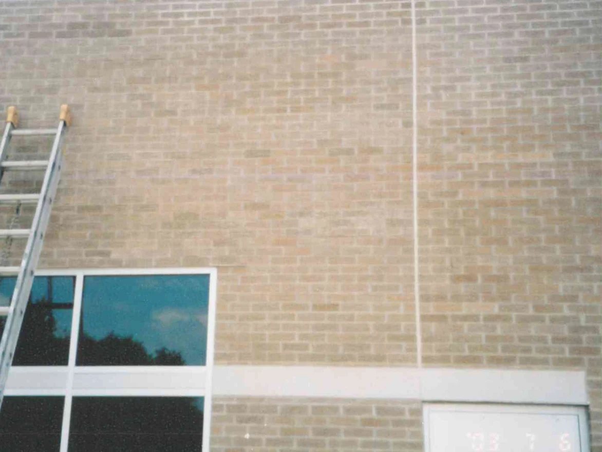 The same wall in July 2003 with an extension ladder leaning against it beside the window, the scattered dark units now closer to the tan of the wall around them