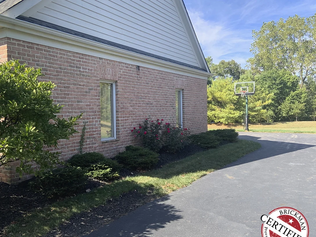 The gable end and side wall seen from the driveway in 2019, the brick reading as one even red range above a planted bed