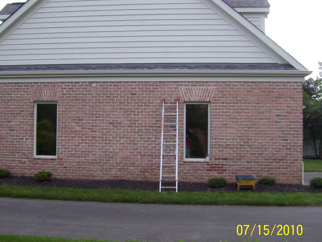 The gable end wall during the work in 2010, an extension ladder leaning against the brick and pale washed patches showing across the courses