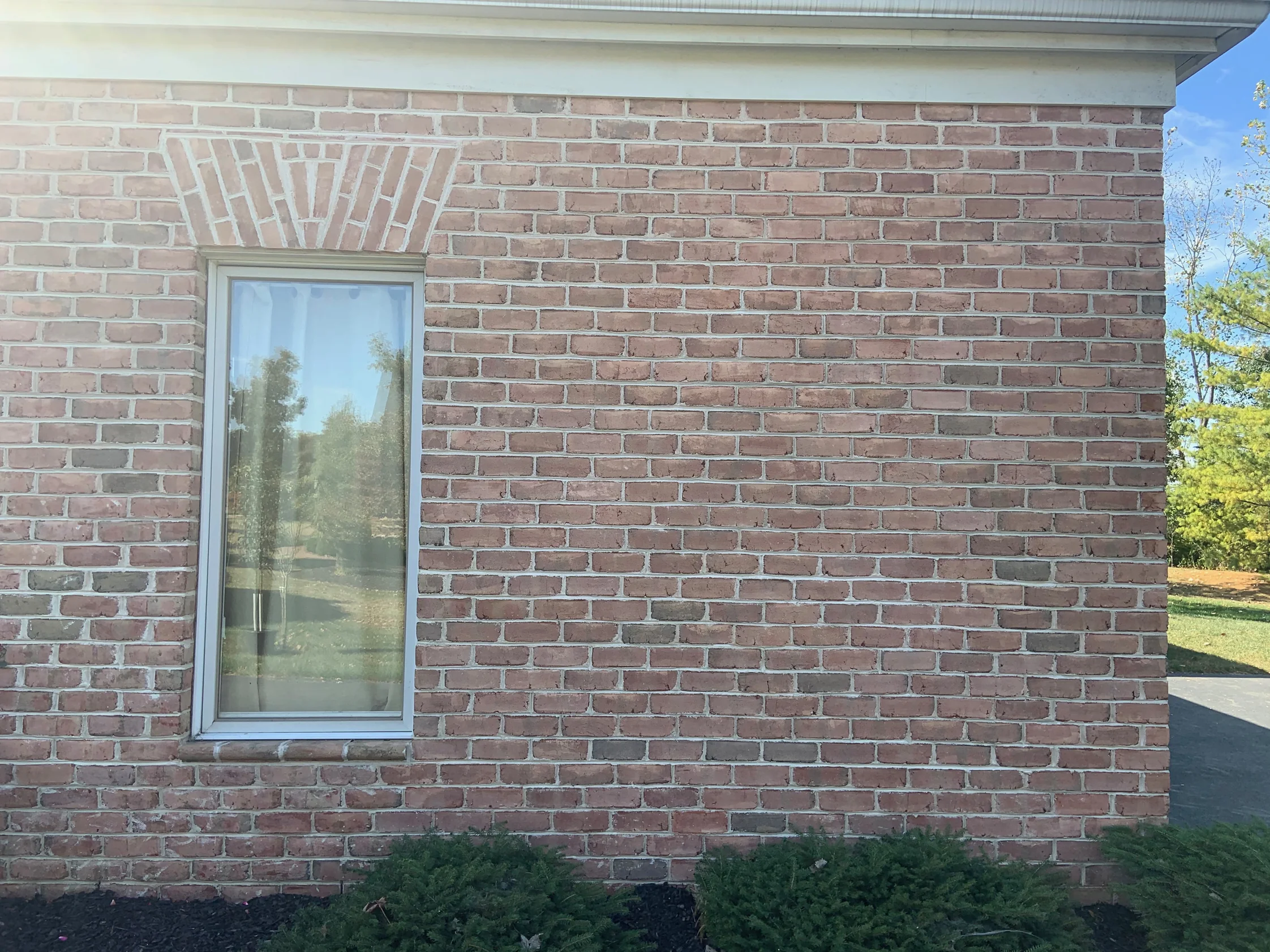 A tall window in 2019 with a fan of brick set above it as a lintel, the wall around it one even red range