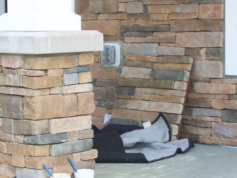 A porch column and the wall behind it before the work in 2012, the stacked stone a pale sandy buff with mixing cups on the slab