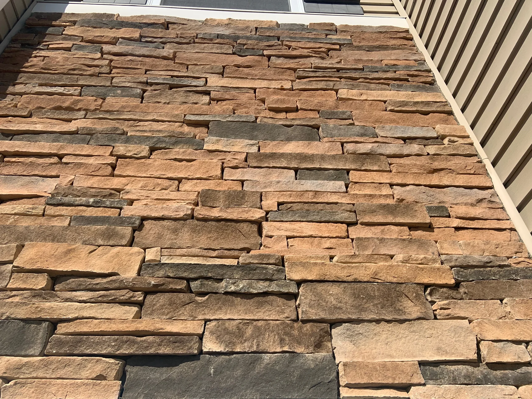 Close view of the stacked stone wall in 2019, the units in mixed tan, rust and grey with tight joints between the courses