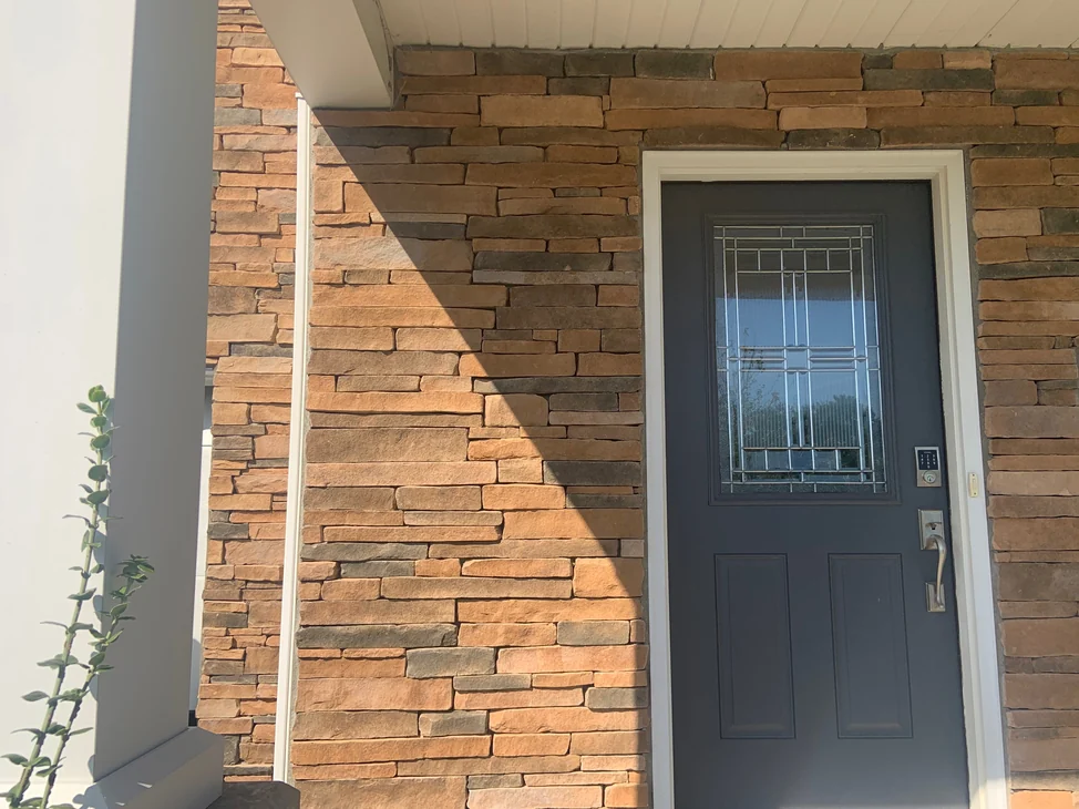 The covered front entry in 2019, the stacked stone around the door reading as one even range of tan, rust and grey.