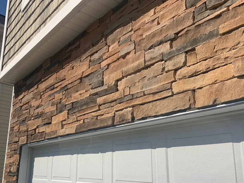 The stone above the garage door in 2019, running under the second-storey shingles in one even tan and rust range
