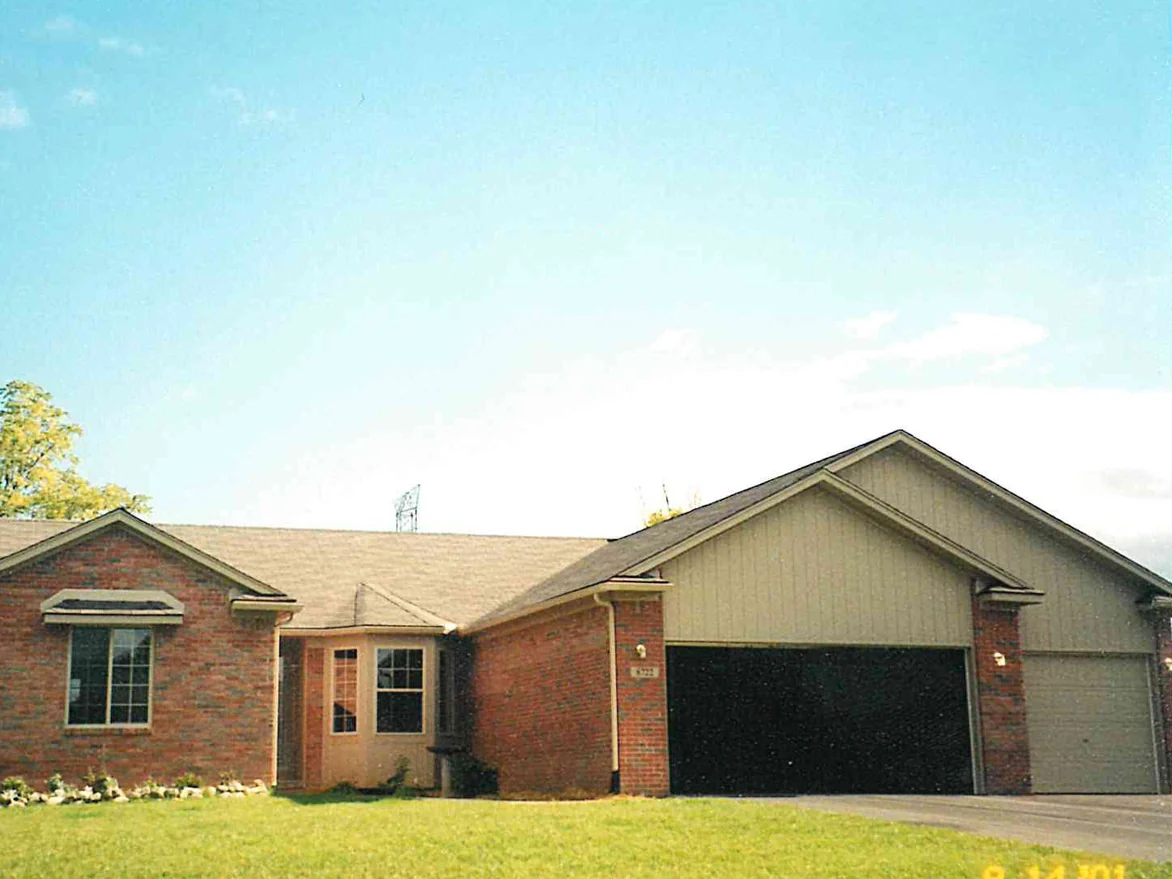 The front of a single-story brick ranch house in 2001, red brick across the entry gable and the wall beside the garage under a tan gable end