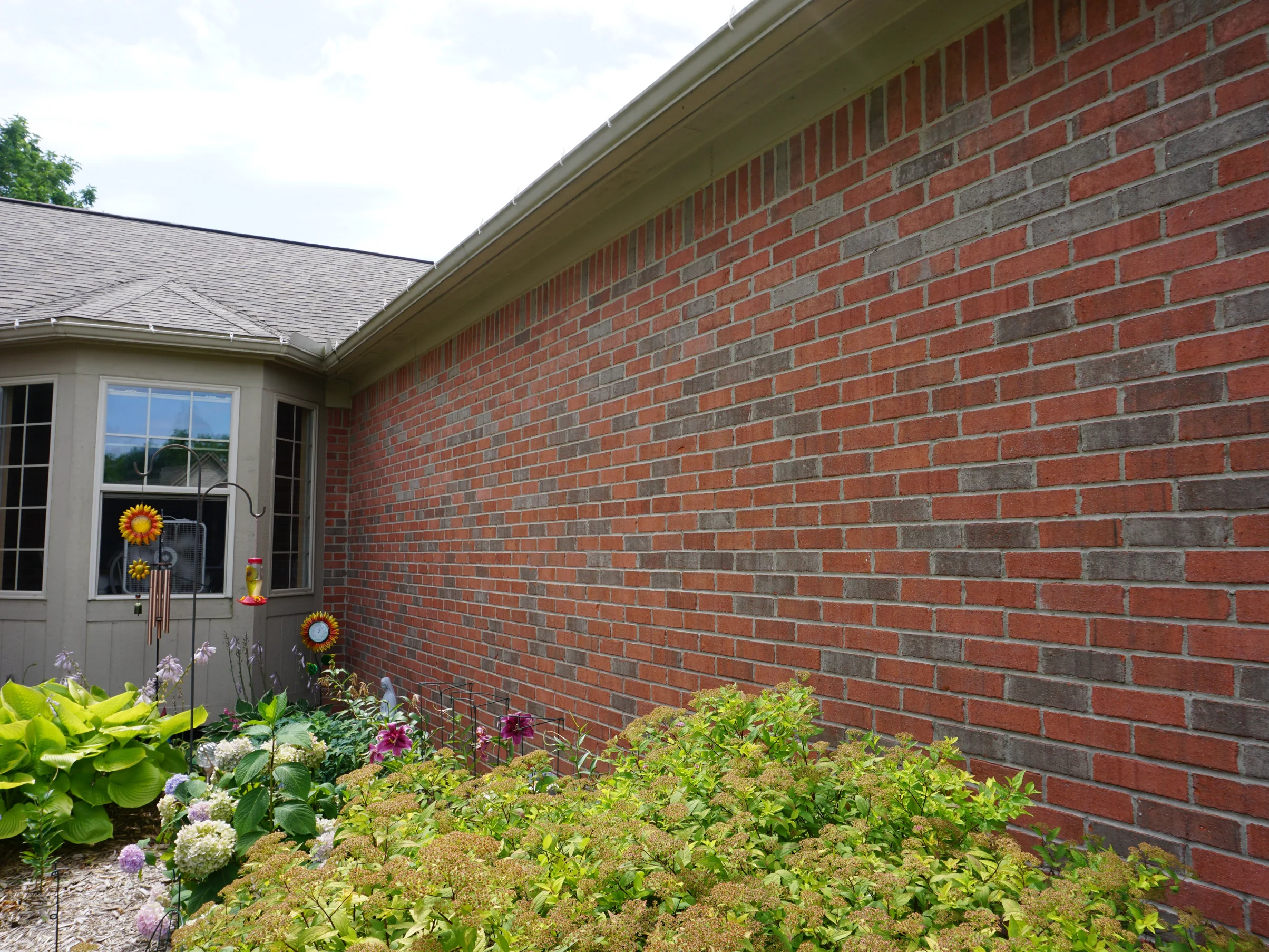 A long side wall of the house in 2019 running from the bay window to the far corner, the brick one even blend of reds, greys and tans