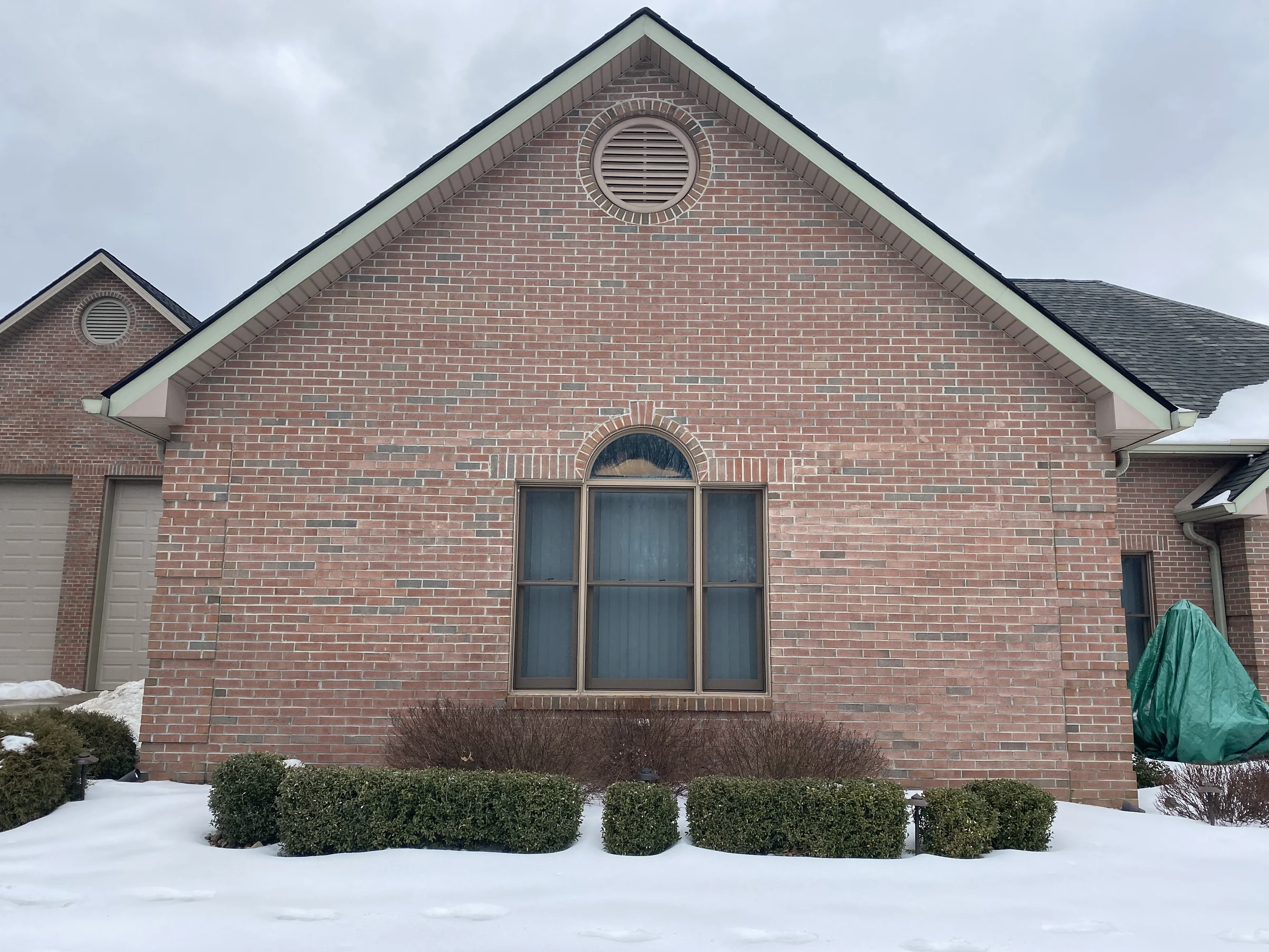 The same gable end straight on in 2021, red brick running evenly from the arched window up to the round louver vent