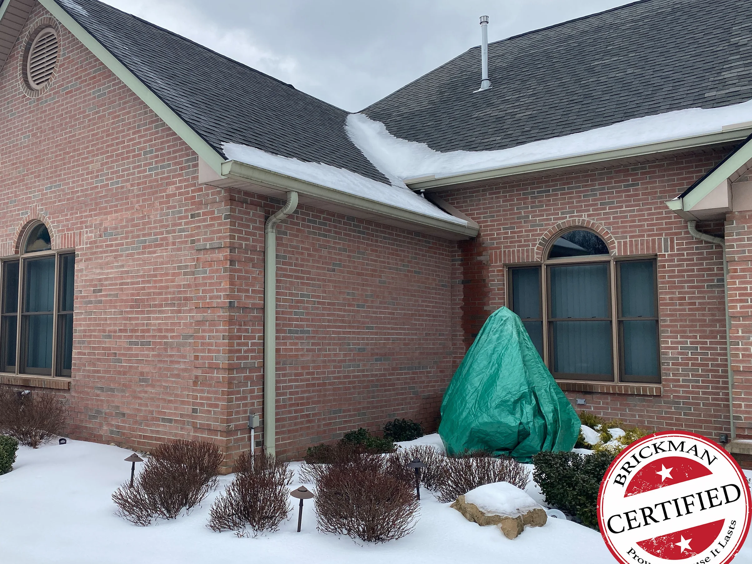 The gable end and the wing beside it in 2021 under snow, red brick reading as one range past the arched windows, with the certification stamp in the corner