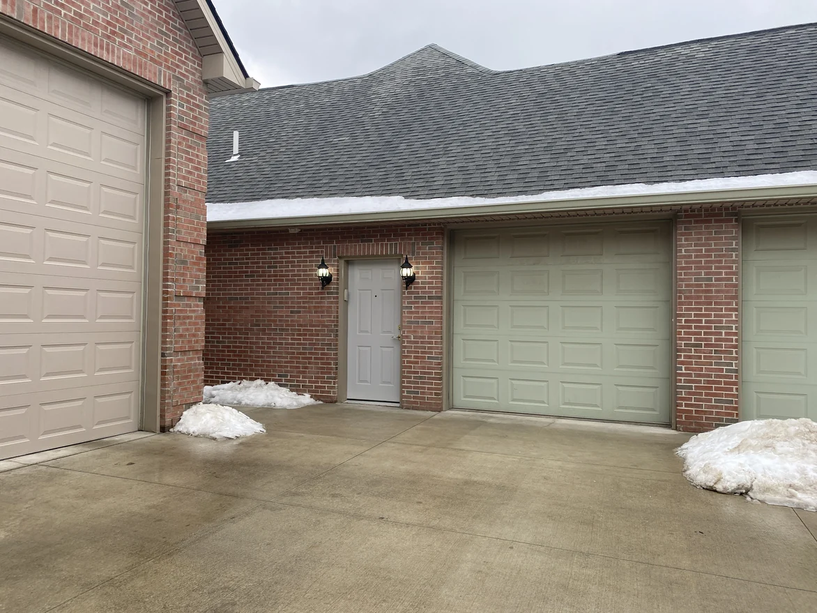 The garage court in 2021, red brick piers standing between the doors and around a service door, snow banked on the concrete
