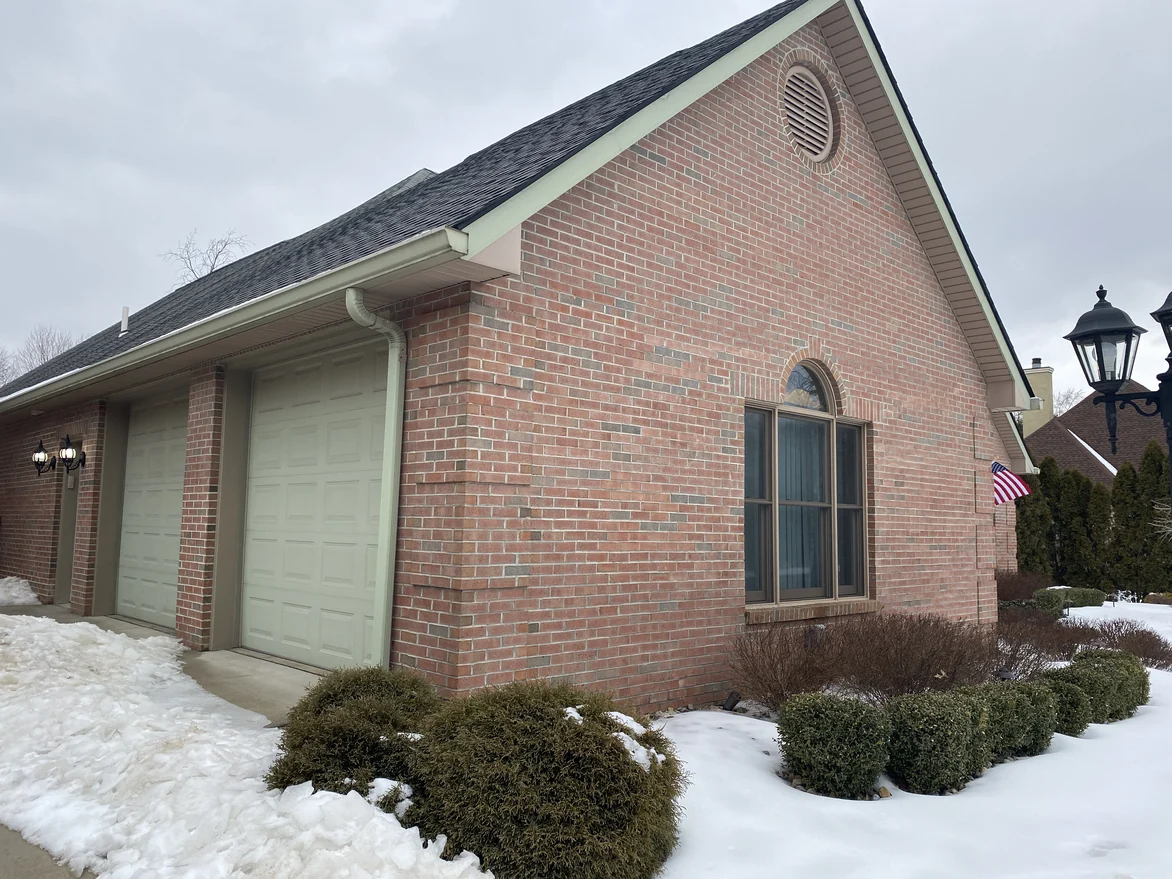 The gable end seen from the driveway in 2021, red brick carrying past the garage bays to the corner under a flag on a bracket