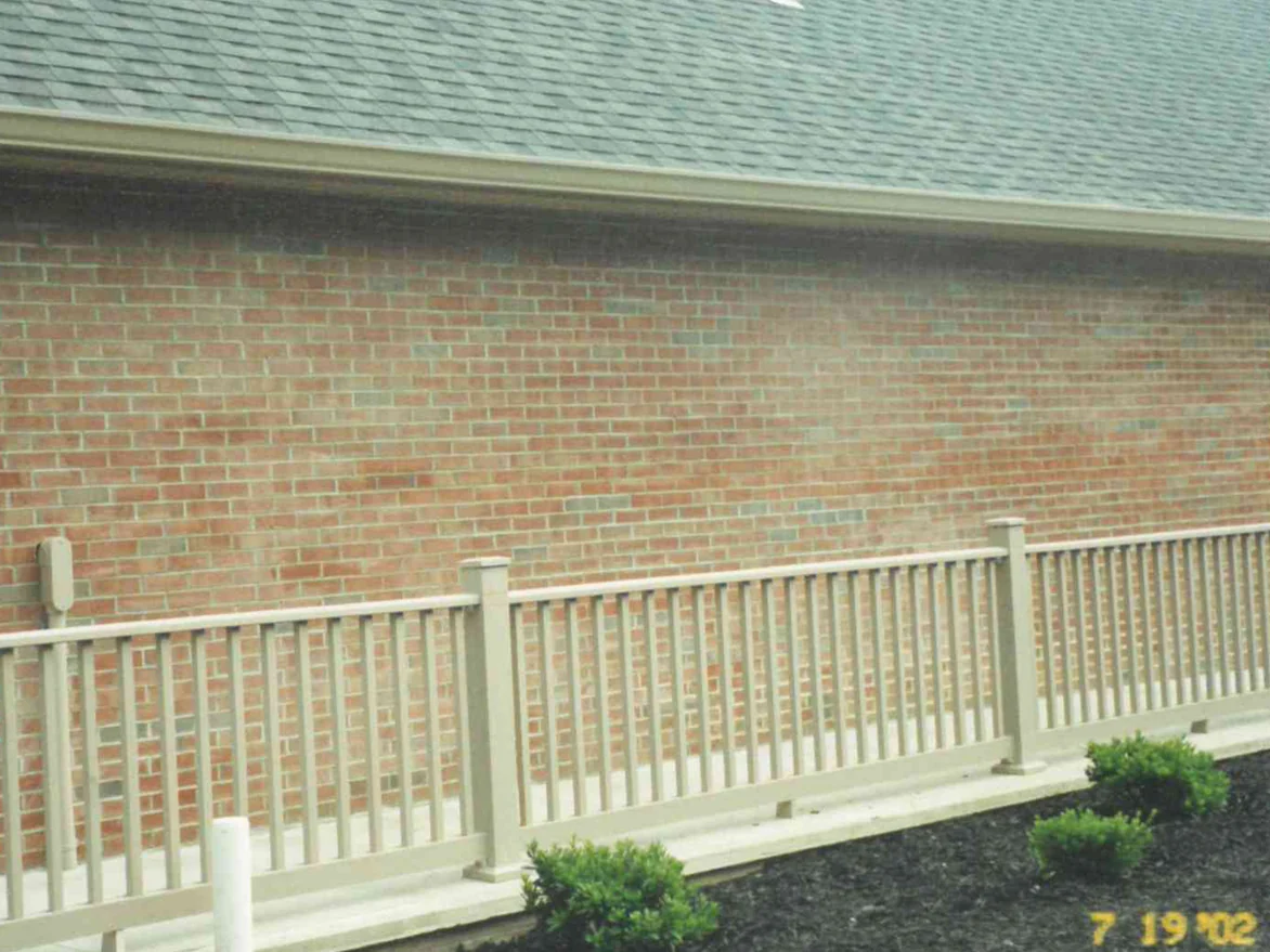 The long side wall of the house in 2002 seen over a deck rail, pale streaks running through the red brick below the eaves