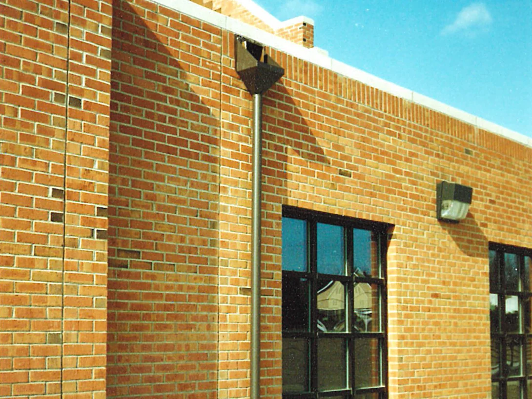 A side elevation in 1995, pale tan brick running past a downspout to a stepped parapet, with darker units through the pilaster