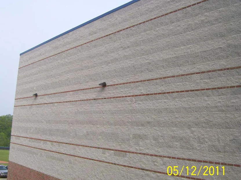 A block wall in 2011 seen along its length, red brick banding crossing split face block of uneven tone above a red brick base and bare dirt