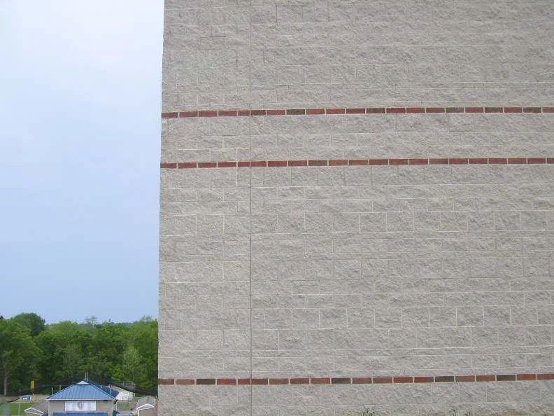 A closer view of the wall in 2011, four red brick banding courses crossing pale split face block, with summer trees and a blue roof past the corner