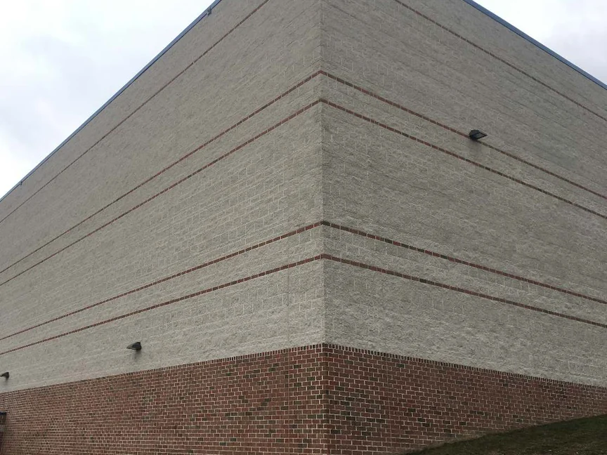 The outside corner of the school in 2021, split face block holding one pale range across both elevations above a red brick base and grass
