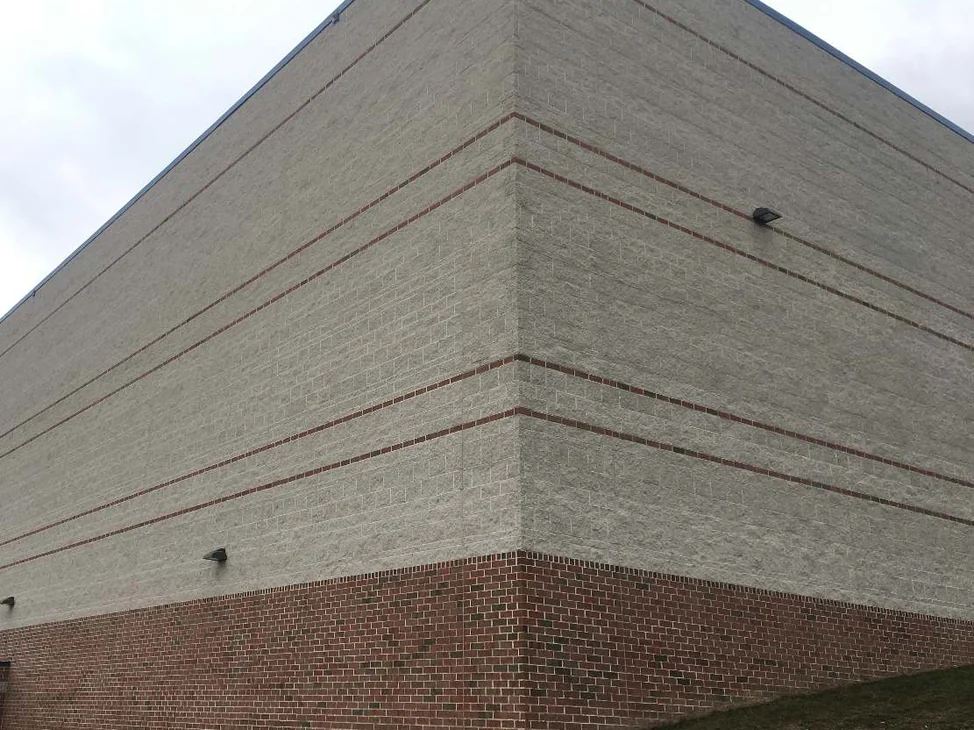 The outside corner of the school in 2021, split face block holding one pale range across both elevations above a red brick base and grass