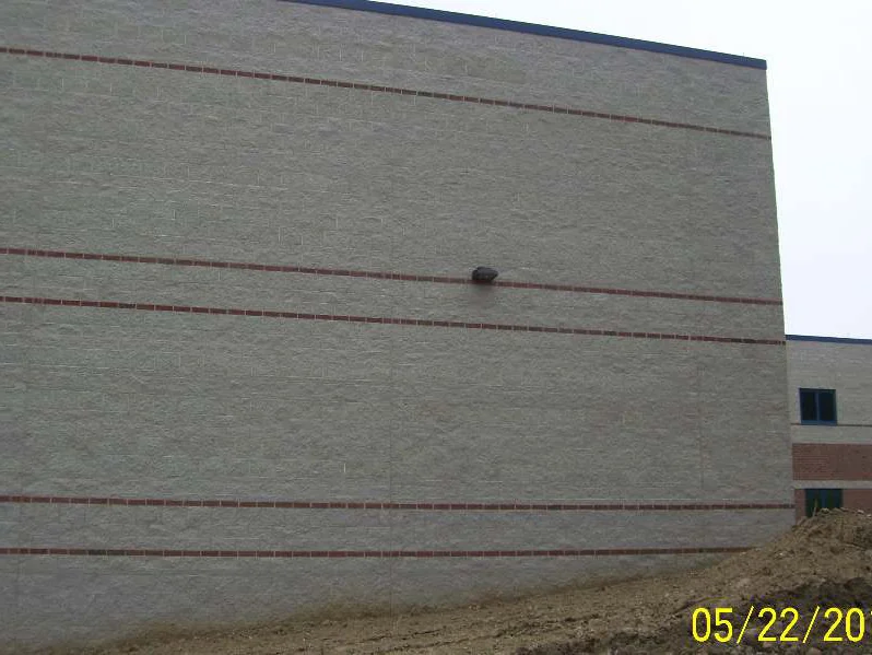The block wall in 2011 reading as one pale range between its red brick bands, a brick classroom wing standing beyond it over open dirt