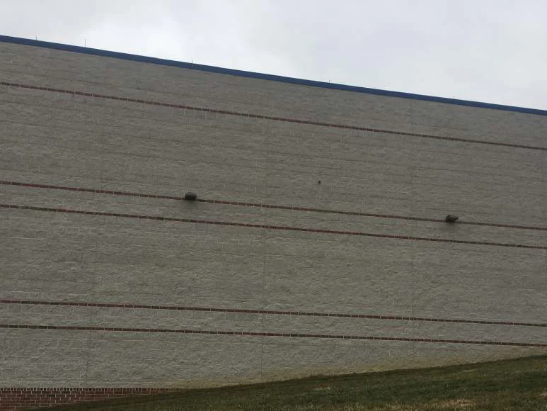 The long elevation in 2021, red brick banding running across pale split face block to a lower brick wing at the right