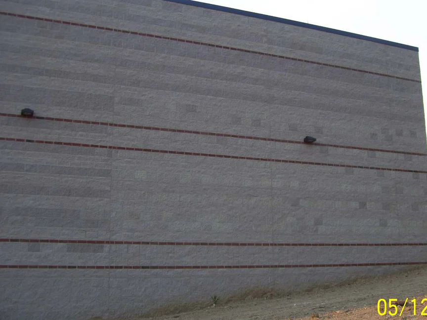 The tall split face block wall in 2011, its grey block mottled dark and pale between thin red brick banding courses, with bare graded dirt at the foot